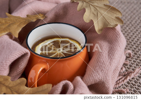 Tea with lemon surrounded by pink blanket and autumn leaves creating warm seasonal atmosphere 131096815