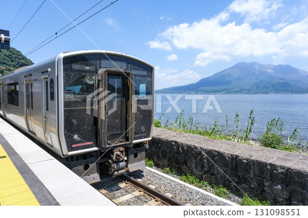 A train stopped at Sengan-en Station, with a view of Sakurajima 131098551