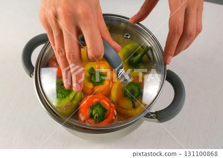 Chef woman cooks covering saucepan with stuffed bell peppers by lid on kitchen. Chef woman cooks covering saucepan with stuffed bell peppers by lid on kitchen. 131100868