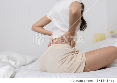 women sitting and pressing her lower back in pain, showing symptoms of backache, muscle strain, or spinal discomfort. Concept of posture, body pain and physical health. 131101255