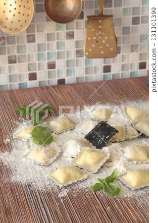 Homemade ravioli with basil leaves on wooden board in kitchen. Healthy eating and organic products. Traditional food, Italy. Brass cutlery. Vintage and old ladle and slotted spoon. 131101399