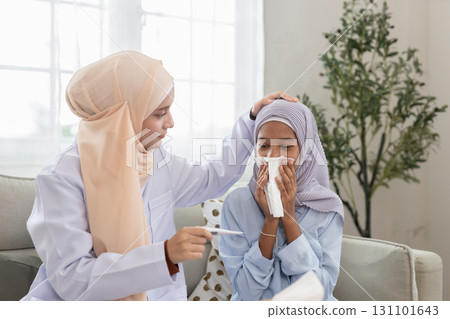 Muslim woman in hijab checking temperature of sick girl at home. Concept of family healthcare, medical care, illness prevention, islamic lifestyle and home treatment. Muslim woman in hijab checking temperature of sick girl at home. Concept of family healthcare, medical care, illness prevention, islamic lifestyle and home treatment. 131101643