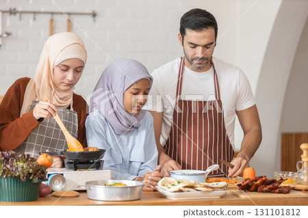 Muslim family cooking together in modern kitchen. Woman in hijab stirring food, child watching, and man preparing ingredients. Concept of halal food, family bonding, healthy lifestyle, and home 131101812