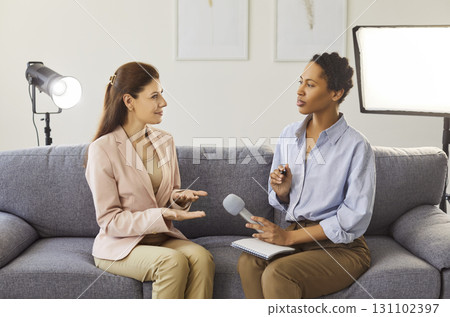 Female interviewer conducting a seated studio interview with microphone and notes Female interviewer conducting a seated studio interview with microphone and notes 131102397