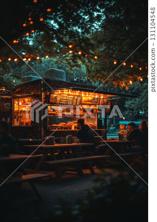 Night food truck scene with string lights, picnic tables, and customers enjoying a meal under the trees 131104548