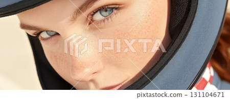 Close-up portrait of a young woman with freckles, intense blue eyes, wearing a blue helmet 131104671