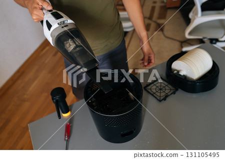 Cropped shot of cleaning company worker male cleaning air humidifier using handheld vacuum cleaner, performing thorough home device maintenance for optimal indoor air quality and cleanliness. Cropped shot of cleaning company worker male cleaning air humidifier using handheld vacuum cleaner, performing thorough home device maintenance for optimal indoor air quality and cleanliness. 131105495