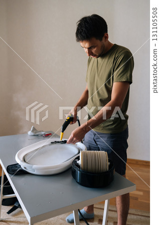 Vertical portrait of housekeeper cleaning air humidifier filter with steam cleaner, washing filter in basin for improved indoor air quality and device performance. Concept of hygiene and household. Vertical portrait of housekeeper cleaning air humidifier filter with steam cleaner, washing filter in basin for improved indoor air quality and device performance. Concept of hygiene and household. 131105508