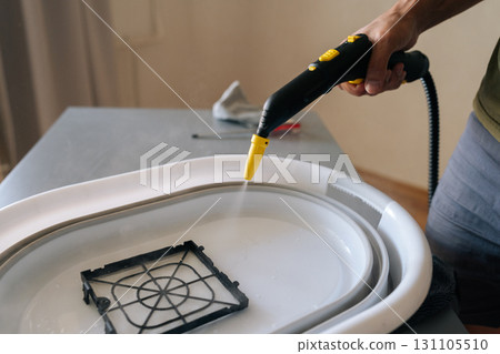Close-up of man using steam cleaner to clean air humidifier filter in basin at home, ensuring regular maintenance for maintaining healthy indoor air quality. Concept of maintenance home appliance. Close-up of man using steam cleaner to clean air humidifier filter in basin at home, ensuring regular maintenance for maintaining healthy indoor air quality. Concept of maintenance home appliance. 131105510