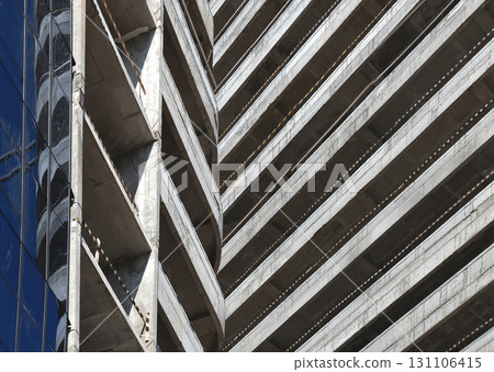 Construction of tall skyscraper. Exposed concrete structure with glass facade, rough balconies, 131106415