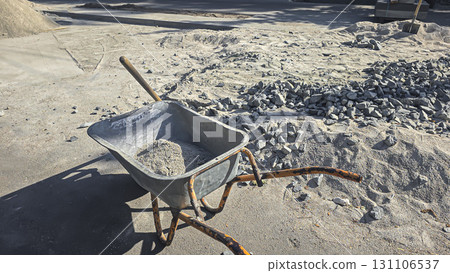 A construction site. A wheelbarrow and shovel, piles of sand and gravel nearby. A construction site. A wheelbarrow and shovel, piles of sand and gravel nearby. 131106537