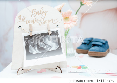 Close-up of ultrasound photo on a small easel with baby shoes and soft decor. Perfect for pregnancy announcements, prenatal content, baby-shower marketing and maternity social posts 131108379