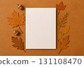 Blank white card on warm ochre background framed by autumn leaves and acorns 131108470