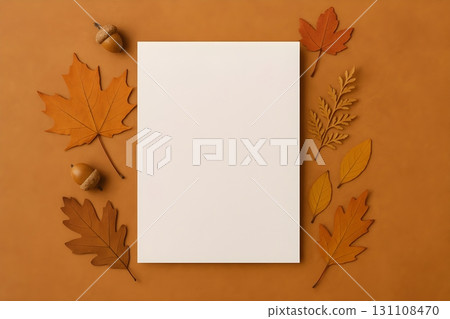 Blank white card on warm ochre background framed by autumn leaves and acorns 131108470