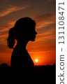Female silhouette in profile with ponytail against glowing orange sunset sky, sun near horizon 131108471