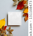 Square blank card on light gray background surrounded by yellow, red, and brown autumn leaves 131108473