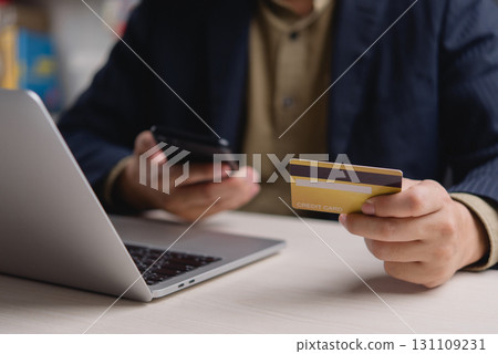 Man holding credit card and smartphone while using laptop, shopping online payment and digital transaction. E-commerce and mobile banking concept. 131109231