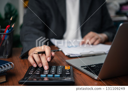 Business person analyzing financial data with paperwork and laptop, showing calculation, expense management, and financial reporting. accounting, budgeting, and tax planning 131109249