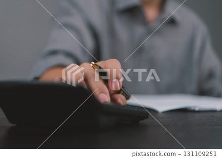 Close-up of hand working with calculator and paperwork, representing tax calculation, financial review, and business expense tracking. Close-up of hand working with calculator and paperwork, representing tax calculation, financial review, and business expense tracking. 131109251
