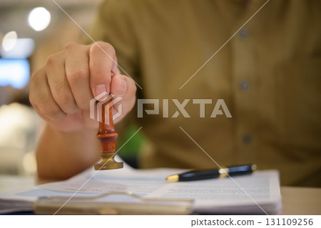 Hand using a rubber stamp on official papers, representing approval process, legal documentation, and certified paperwork. contract certification, notarization, and business authorization. Hand using a rubber stamp on official papers, representing approval process, legal documentation, and certified paperwork. contract certification, notarization, and business authorization. 131109256