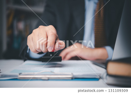 Businessman stamping contract document on desk, symbolizing legal approval, corporate agreement, and business authorization process. 131109309