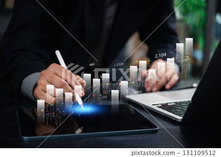 businessman analyzing financial data and growth trends on a tablet with digital graphs and charts, working on a laptop in a modern office. 131109512