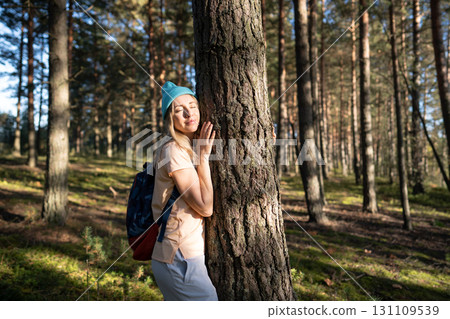 Loving nature purity. Relaxed woman touching tree trunk in autumn forest with closed eyes at sunset. Loving nature purity. Relaxed woman touching tree trunk in autumn forest with closed eyes at sunset. 131109539