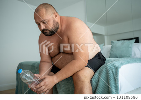 Obesity problem. Depressed fat man sadly holding bottle water feeling solitude personal life trouble 131109586