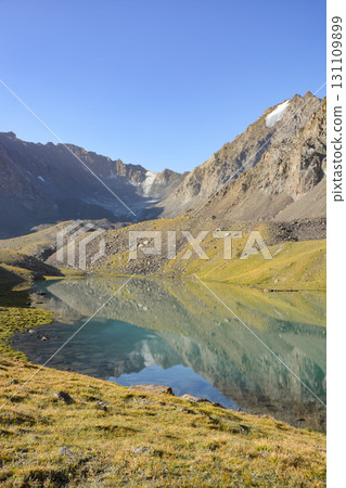 Idyllic summer landscape with hiking trail in the mountains with beautiful fresh green mountain pastures, lake with reflection. Alai ridge mountains Idyllic summer landscape with hiking trail in the mountains with beautiful fresh green mountain pastures, lake with reflection. Alai ridge mountains 131109899