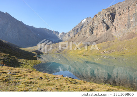 Idyllic summer landscape with hiking trail in the mountains with beautiful fresh green mountain pastures, lake with reflection. Alai ridge mountains Idyllic summer landscape with hiking trail in the mountains with beautiful fresh green mountain pastures, lake with reflection. Alai ridge mountains 131109900