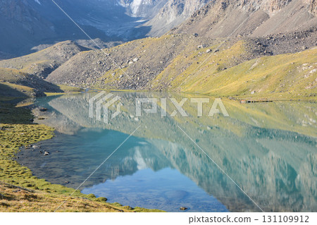 Idyllic summer landscape with hiking trail in the mountains with beautiful fresh green mountain pastures, lake with reflection. Alai ridge mountains 131109912