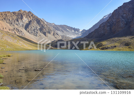 Idyllic summer landscape with hiking trail in the mountains with beautiful fresh green mountain pastures, lake with reflection. Alai ridge mountains Idyllic summer landscape with hiking trail in the mountains with beautiful fresh green mountain pastures, lake with reflection. Alai ridge mountains 131109916