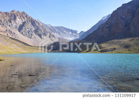 Idyllic summer landscape with hiking trail in the mountains with beautiful fresh green mountain pastures, lake with reflection. Alai ridge mountains Idyllic summer landscape with hiking trail in the mountains with beautiful fresh green mountain pastures, lake with reflection. Alai ridge mountains 131109917