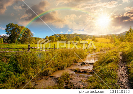 mountainous rural landscape in autumn at sunset. wooden fence near the path through grassy meadow on the hillside. scenery with fir forest on the mountains in evening light under sky with clouds 131110133
