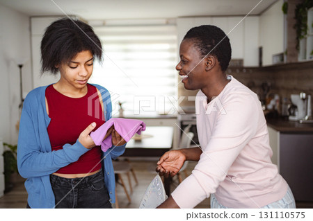 Mother and daughter ironing clothes and smiling at home Mother and daughter ironing clothes and smiling at home 131110575