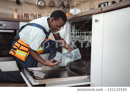 Repairman examining dishwasher filter in kitchen 131110585