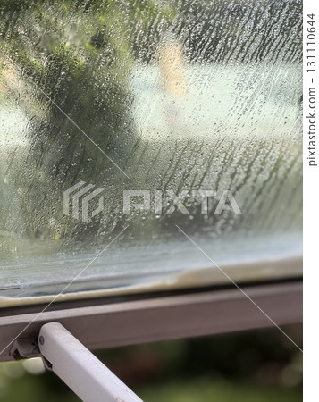 Raindrops on window creating a textured background with blurred green foliage in the distance 131110644