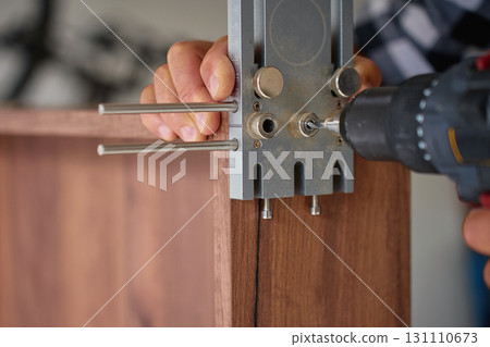 Carpenter drilling wooden panel using jig tool for precise holes Carpenter drilling wooden panel using jig tool for precise holes 131110673