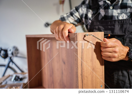 Man assembling wooden furniture using Allen key for in workshop 131110674