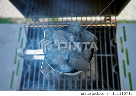 Burning charcoal briquettes in chimney starter on grill top view Burning charcoal briquettes in chimney starter on grill top view 131110713