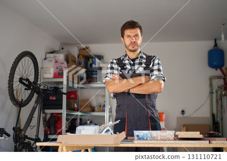 Carpenter standing with crossed arms in home workshop with tools and materials 131110721