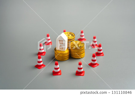 Stacked coins and house surrounded by traffic cones. Asset freeze, financial sanctions, foreclosure risks, and restrictions on property investments due to economic or legal barriers. 131110846