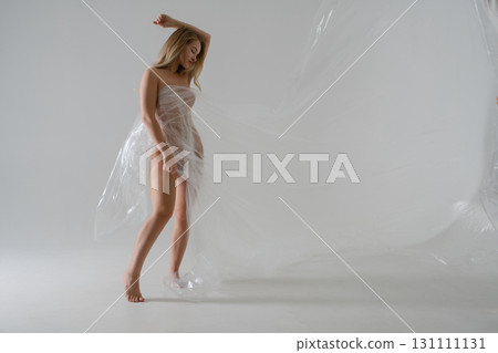 Elegant blonde woman in beauty shoot with plastic draping in studio setting 131111131