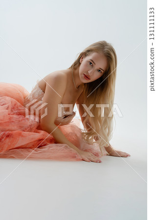 Blonde woman poses in studio wearing elegant dress with flowing fabric Blonde woman poses in studio wearing elegant dress with flowing fabric 131111133