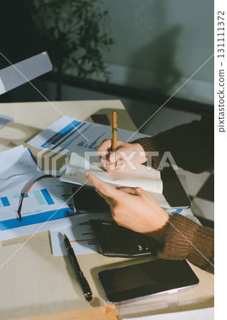 Close-up of businessman's hands making notes, mobiles, chart, desk, office 131111372
