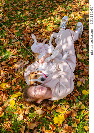 Girl lying on autumn leaves with her dog, looking at camera. Happy pet owner. 131111494