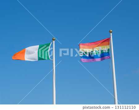 Ireland and pride rainbow flag waving on flagpoles against clear blue sky in West Cork. Ireland and pride rainbow flag waving on flagpoles against clear blue sky in West Cork. 131112110