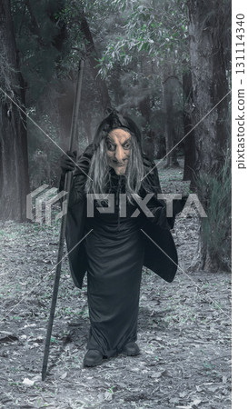 Old witch woman walking through the forest with a stick. The scene is scary and creepy. Concept of Spooky Halloween 131114340