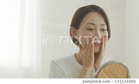 一位 40 多歲的日本女性對著鏡子檢查自己的皮膚狀況 131114368
