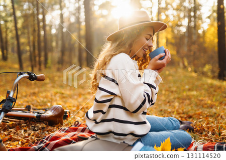 Relax in forest Woman sits on blanket, drinks from thermos, enjoys autumn atmosphere in sunny forest Relax in forest Woman sits on blanket, drinks from thermos, enjoys autumn atmosphere in sunny forest 131114520